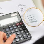 Close-up Of Businessperson Investigating Bills With Magnifying Glass And Calculator